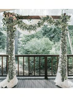 an outdoor wedding ceremony setup with greenery and white draping on the balcony