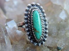 "This is a fine example of an early 60s Bell Trading Company Native American sterling ring. The piece has a striking slim oval turquoise cabochon in an aqua shade with beautiful figuring and a touch of golden brown. The stone is set with a serrated bezel, bordered in a wire twist and finished with silver studs that form a scalloped border. The shank splits into a V at the shoulders, and attaches securely underneath the mounting. The ring is in very nice vintage condition, and measures as a size Flower Cuff Bracelet, Vintage Native American Jewelry, Belle Silhouette, Scalloped Border, Early 60s, Rope Twist, Native American Turquoise, Trading Post, Silver Band Ring