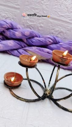 there is a small metal candle holder with three candles on it and purple yarn in the background