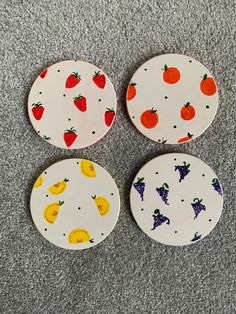 four plates with fruit designs on them sitting on the floor in front of a gray carpet