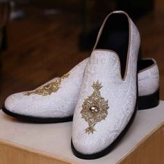 a pair of white slippers with gold embellishments on top of a wooden block