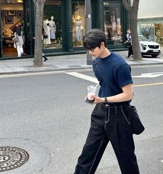 a young man walking down the street with his cell phone in his hand and wearing black pants