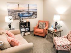 a living room with two orange chairs and a blue boat painting on the wall behind them