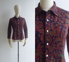 "A kitschy 1970's blouse. Collared jersey knit shirt in a vibrant baroque floral print.  The colors are a mix of deep navy blue, olive green & bright red. Features a tailored skimming fit, three quarter sleeves & silver buttons down the front.  No fabric labels - appears to be a silk jersey/polyester knit material. Best fits an XS-S.  Mannequin is a Size S (34-26-35), top fits as shown. Measures 17\" across the chest, has stretch to 18\".  Recommended for 33-35\" bust comfortably.  Total length Vintage Fitted Paisley Print Tops, Fitted Shirt With Vintage Print For Fall, Fitted Shirt With Retro Print For Fall, Fitted Paisley Print Top For Fall, Fitted Long Sleeve Tops With Vintage Pattern, Fitted Red Top With Vintage Print, 1970s Fitted Long Sleeve Tops, 1970s Blouse, Baroque Floral