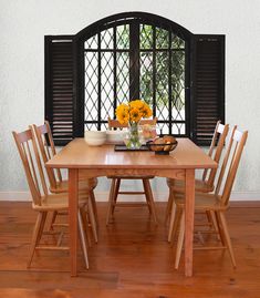 a wooden table with four chairs and two vases filled with sunflowers in front of an arched window