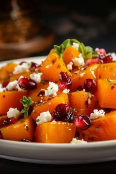 a white plate topped with carrots and cheese covered in pomegranate, garnished with fresh herbs