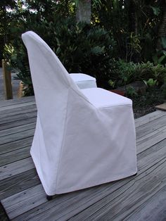 a white chair sitting on top of a wooden deck next to bushes and trees in the background