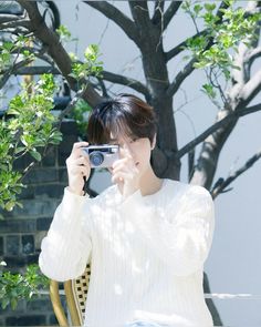 a woman is taking a photo with her cell phone while sitting in a chair under a tree