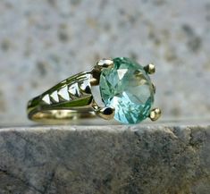 This beautiful and elegant sea foam green spinel ring holds true to the timeless designs of the late 1960's Mid-century period. The lines are strong and romantic, with just the right curves and flash to catch your eye. A 10 karat gold setting accentuates a large, light green synthetic spinel solitaire. Shifts and changes to the light and color give this ring a rich organic feel with layers of brightness and sparkle. Such an outstanding piece for any green stone lover! The stone measures 9mm and has great flashes of teal, mint and aqua. The rise off the finger measures 6.6mm. This beautiful piece has been well cared for and shows no large chips to the center stone. The inside of the band is no longer stamped but tests as 10 karat gold. The band has a nice thickness and the stone is secure i Antique Green Emerald Ring With Prong Setting, Art Deco Emerald Ring With Round Diamond Cut, Green Amethyst Rings For Wedding, Green Topaz Ring With Center Stone, Formal Green Sapphire Ring With Center Stone, Heirloom Green Emerald Solitaire Ring, Heirloom Green Sapphire Ring For May Birthstone, Art Deco Green Emerald Ring With Diamond Cut, Green Round Topaz Ring For Anniversary