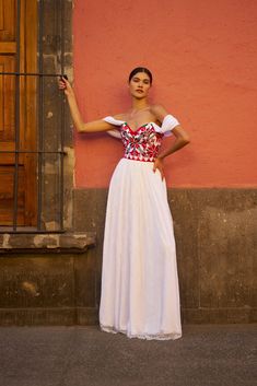 a woman standing in front of a pink wall wearing a white dress and holding her hand up