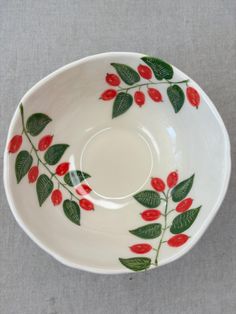 a white bowl with red berries and green leaves painted on the side, sitting on a gray surface