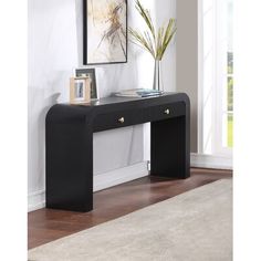 a black console table with two drawers and a vase on it in front of a white wall