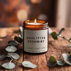 a candle sitting on top of a wooden table next to eucalyptus leaves and greenery