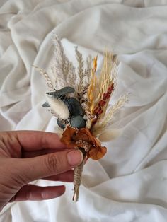 a hand holding a dried flower on top of a white cloth covered bedding area