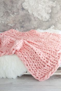 a pink blanket on top of a bed next to a white fluffy rug and wall