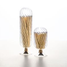 two glass vases sitting on top of a white table next to each other with sticks sticking out of them