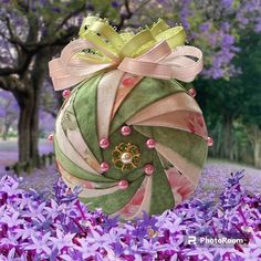 an ornament in the shape of a ball with ribbons and pearls on it surrounded by purple flowers