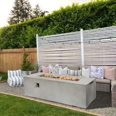 an outdoor fire pit in the middle of a yard with pillows and cushions on it