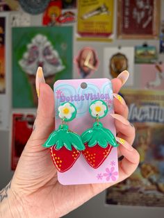 a person holding up a cell phone case with two strawberry shaped earrings on top of it