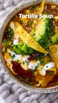 an overhead view of a bowl of soup with avocado, sour cream and other toppings