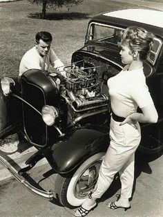 an old black and white photo of two people looking at a car engine