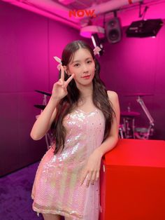 a girl in a pink dress posing for the camera with her finger up to her ear