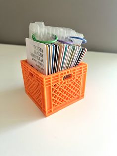 an orange plastic container filled with lots of different types of papers on top of a white table