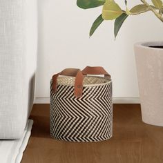 a black and white basket sitting on top of a wooden floor next to a potted plant