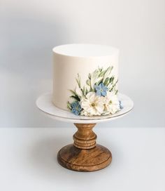 a white and blue floral decorated cake on a wooden stand, with the top half covered in frosting