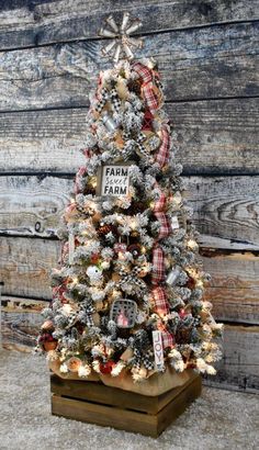 a small christmas tree with red and white plaid ribbon on it, sitting in front of a wooden wall