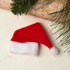 a red and white santa hat laying on top of a table next to pine branches