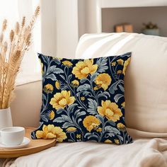 a blue and yellow floral pillow sitting on top of a couch next to a cup