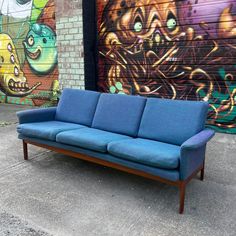 a blue couch sitting in front of a wall with graffiti on it's side