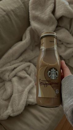 a person holding up a bottle of starbucks frappresse coffee in front of a couch