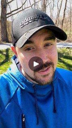 a man with a mustache wearing a blue jacket and black hat in front of trees