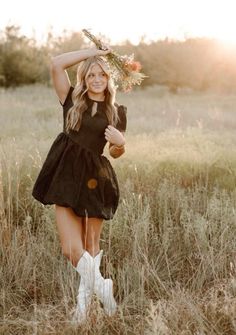 a woman in a black dress and white cowboy boots posing for a photo with her arms behind her head