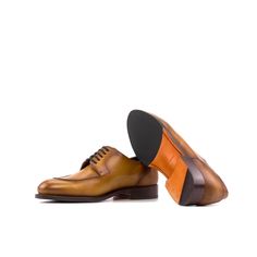 a pair of brown and orange shoes on top of a white background with an orange sole