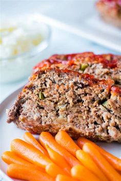 meatloaf and carrots on a white plate with other food in the background