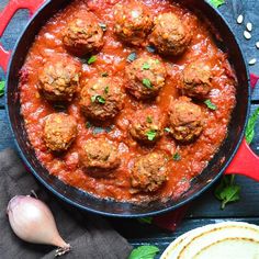 meatballs and sauce in a skillet on a wooden table next to some garlic