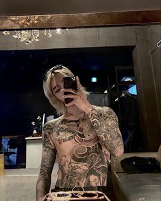 a tattooed man taking a selfie in front of a mirror with his cell phone