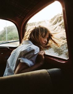 a woman sitting in the back seat of a car with her hair blowing in the wind