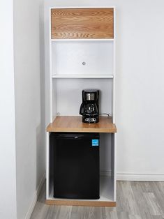 a black coffee maker sitting on top of a wooden table next to a white shelf