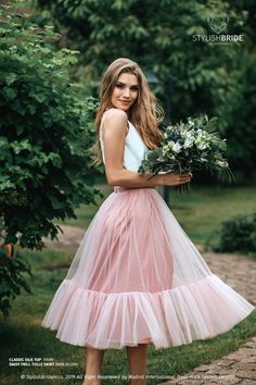 a woman in a pink dress holding flowers and posing for the camera with her hands on her hips