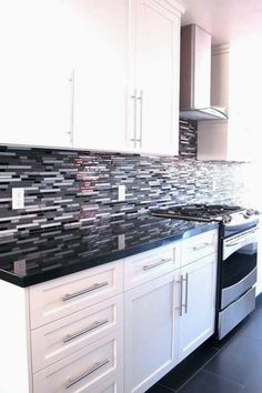 a kitchen with white cabinets, black counter tops and silver backsplash tiles on the wall