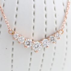 This timelessly gorgeous diamond necklace showcases brilliant white diamonds set in a lustrous 14k rose gold curved 7 stone pendant setting creating an eye-catching and chic look. The 7 diamond pendant hangs gorgeously from a solid 14k rose gold cable chain. The length of the gold chain can be adjusted to either 16" or 18" long to suit your style! This curved diamond necklace matches perfectly with our seven diamond wedding band and earrings. It can be made in your choice of white, rose, or yell Dazzling Rose Gold Necklace With Prong Setting, Dazzling Rose Gold Necklace With Cubic Zirconia, Dazzling Rose Gold Diamond Necklace, Elegant 14k Rose Gold Pendant Necklace, Dazzling 14k Rose Gold Necklace, Cubic Zirconia Rose Gold Necklace For Anniversary, Rose Gold Diamond Necklace For Anniversary, Dazzling Rose Gold Diamond Necklace With Accents, Dazzling Rose Gold Diamond Accents Necklace