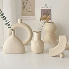 some white vases are sitting on a table next to each other and one has a plant in it