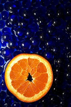 an orange cut in half sitting on top of blue glass balls with water droplets around it