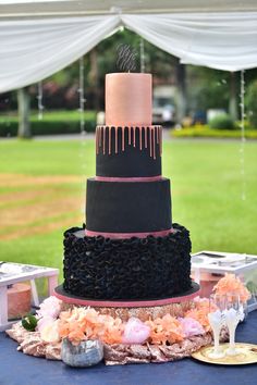 a black and pink wedding cake sitting on top of a blue tablecloth covered table