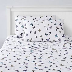 a white bed topped with lots of butterflies on it's cover and pillow cases