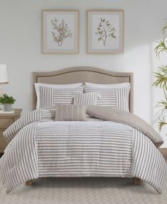 a bed with white and grey striped comforter in a bedroom next to two framed pictures